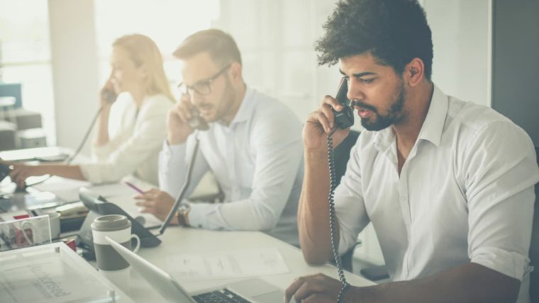 Employees in a Dallas-Fort Worth office using desk phones and laptops — representing the business communication environment NTI Technologies cloud phone systems are designed to support