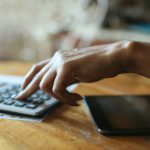 Person using a calculator and tablet to calculate insurance premium savings from a commercial security system for a Dallas-Fort Worth business