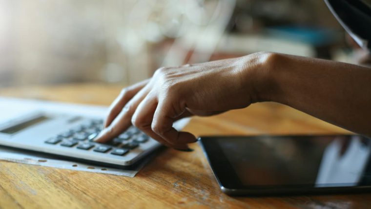 Person using a calculator and tablet to calculate insurance premium savings from a commercial security system for a Dallas-Fort Worth business