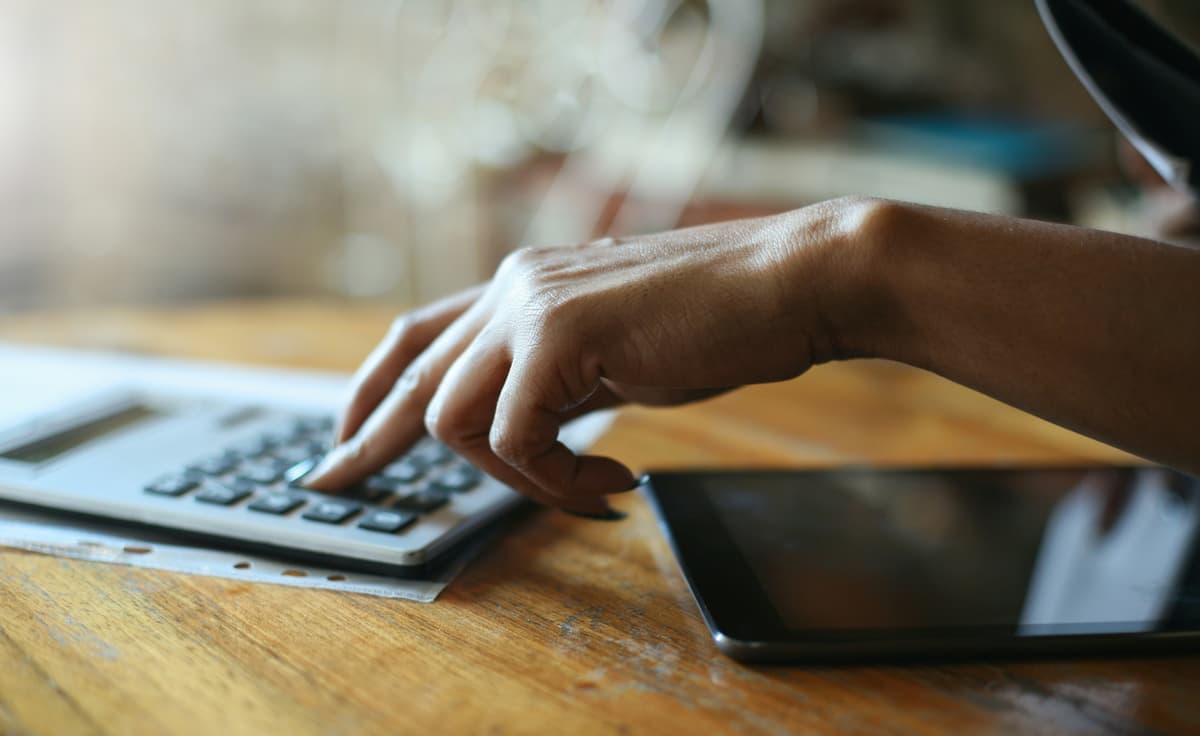 Person using a calculator and tablet to calculate insurance premium savings from a commercial security system for a Dallas-Fort Worth business