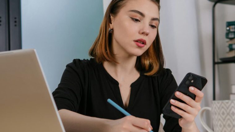 Business professional comparing hosted phone system vs traditional PBX costs on mobile device while taking notes in Dallas Fort Worth office