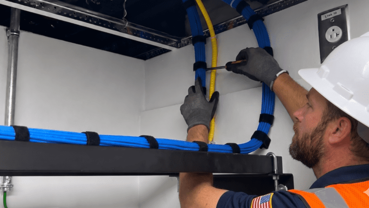 Technician organizes network cables against a white wall.
