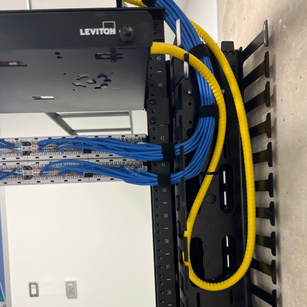 Rear view of Leviton patch panels showing blue Cat6 and yellow fiber cable terminations with vertical cable manager