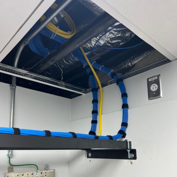 Bundled blue Cat6 and yellow fiber cables routed from ceiling cable ladder tray down into the IDF room infrastructure