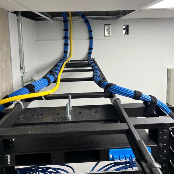 Blue Cat6 and yellow fiber cable bundles neatly dressed and velcro-strapped along an overhead ladder tray above a network rack