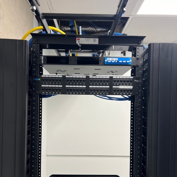 Cat6 patch panels with labeled ports installed in a Leviton rack, with fiber enclosure and overhead cable management