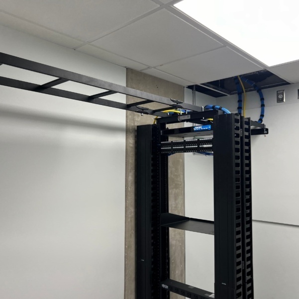 Open-frame network rack with structured Cat6 and fiber cabling routed through overhead cable tray in a commercial IDF room