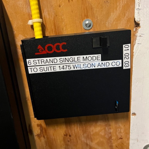 OCC 6-strand single mode fiber enclosure labeled for Suite 1475 Wilson and Co, mounted on plywood backboard