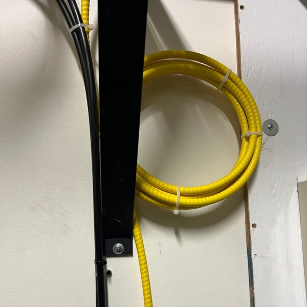 Neatly coiled yellow OS2 armored fiber optic cable secured with cable ties on a wall-mounted rack