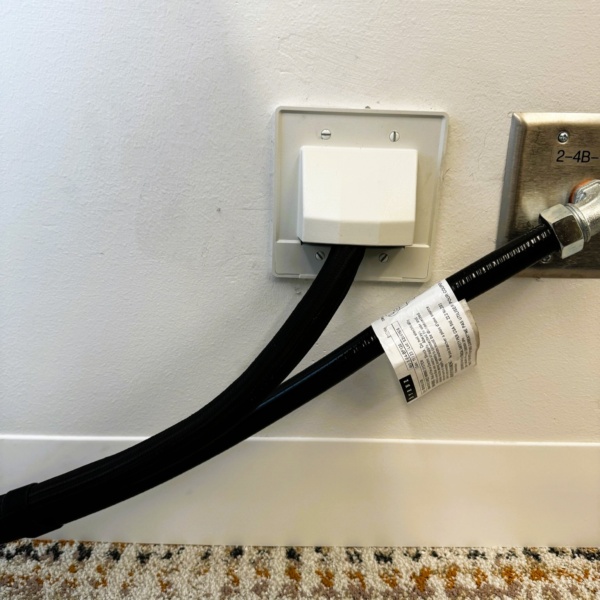 Cable connection entering a wall plate beside labeled electrical conduit.