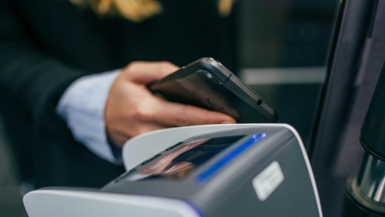 Access control credentials Dallas — person tapping a smartphone to an NFC reader as a mobile access control credential, representing the mobile credential options NTi Technologies configures through Brivo and Avigilon Alta for DFW commercial offices