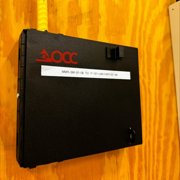 Labeled OCC fiber enclosure mounted on a plywood backboard.