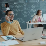 Small business owner using cloud phone system on mobile at laptop in Dallas-Fort Worth office