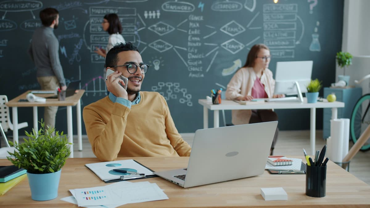 Small business owner using cloud phone system on mobile at laptop in Dallas-Fort Worth office