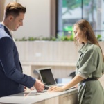 Visitor management system Dallas — business visitor checking in at a modern commercial office reception desk, representing the digital visitor management systems NTi Technologies installs for DFW offices